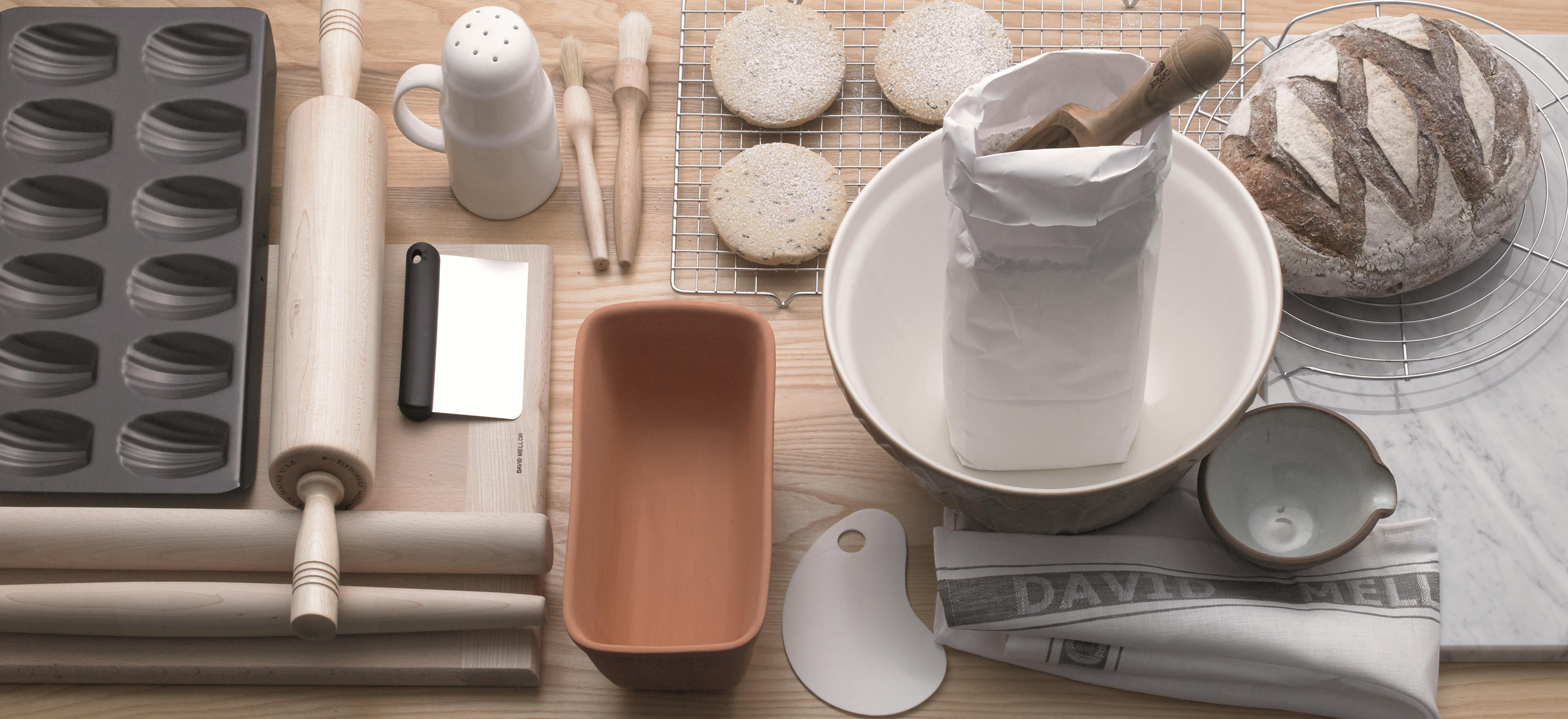 Baking items such as a rolling pin, pastry board, cooling rack displayed on a work top.