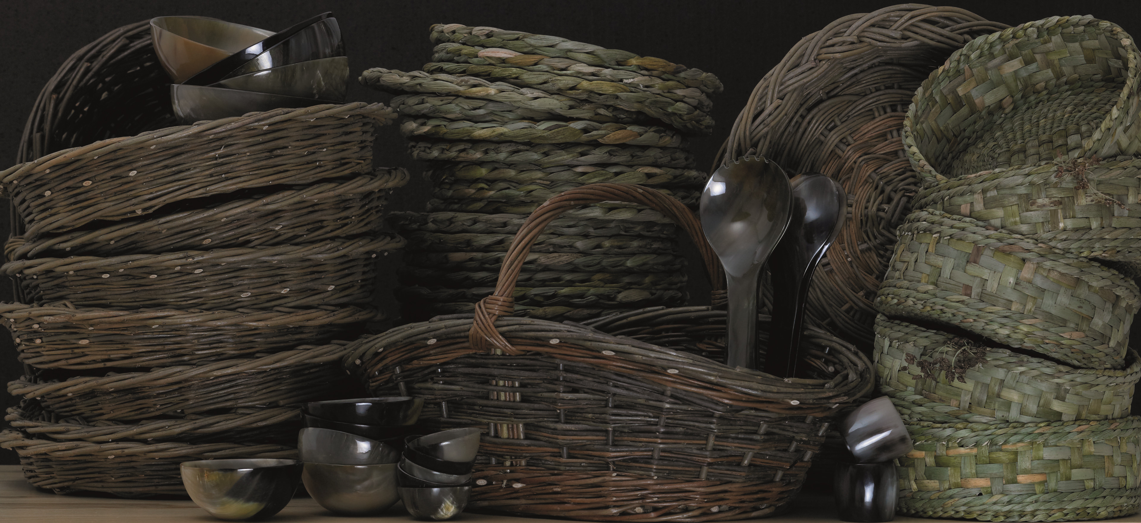 Craft basketware items stacked on a table with horn salad servers protruding from the Vegetable Gatherer basket.