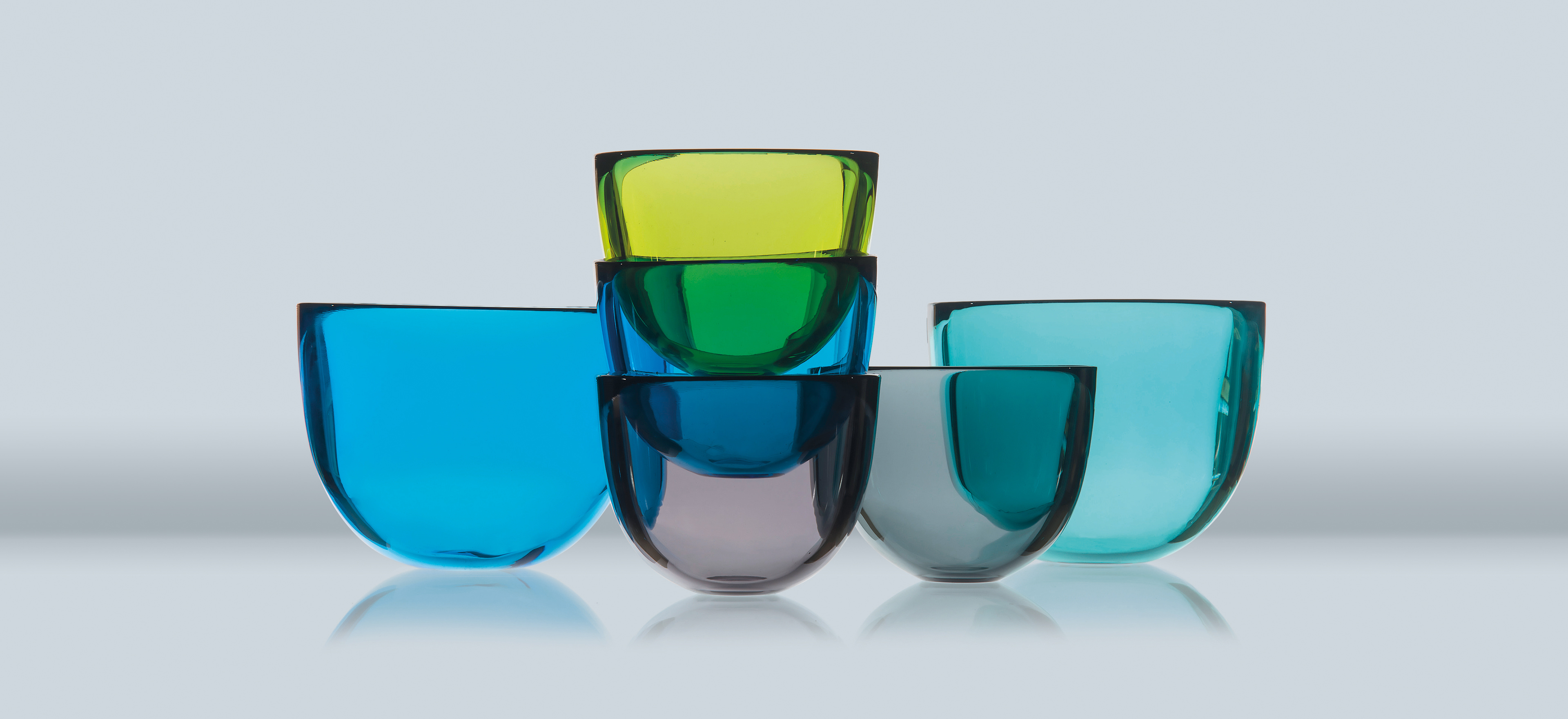 Various sizes of the David Mellor glass bowl/candleholder arranged on a grey background.