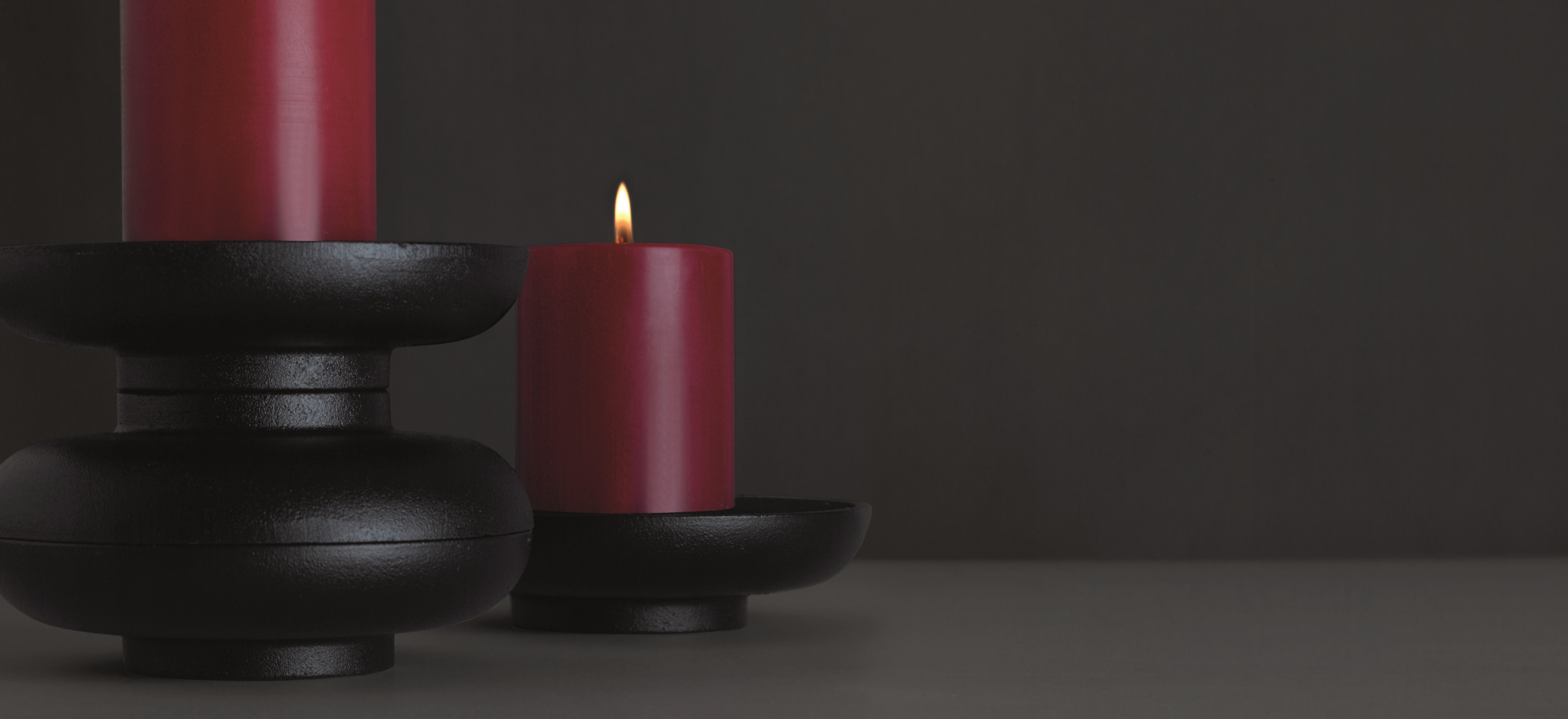 The David Mellor cast iron candleholder with red candle on a dark grey background.