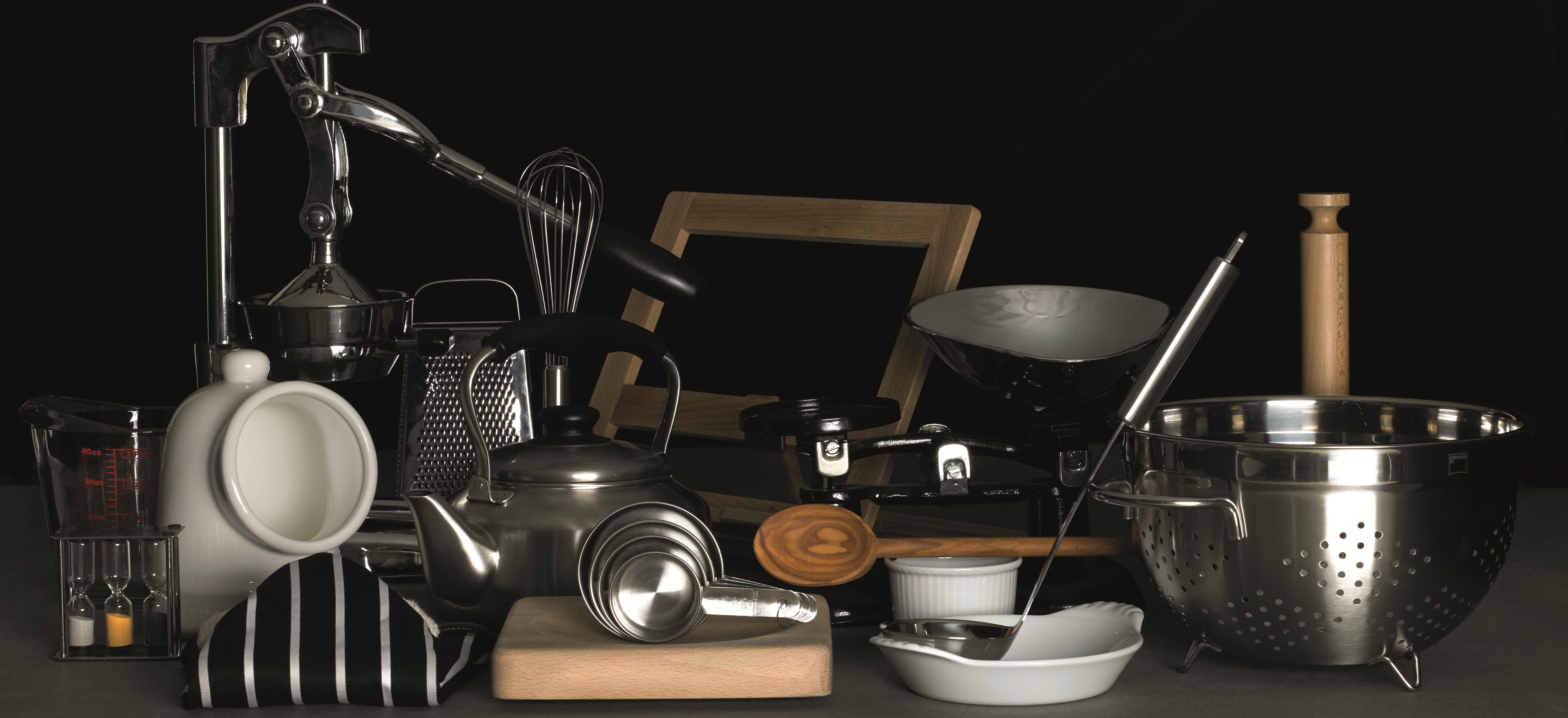 Kitchen essentials such as kettles, colanders and whisks arranged on a black background.