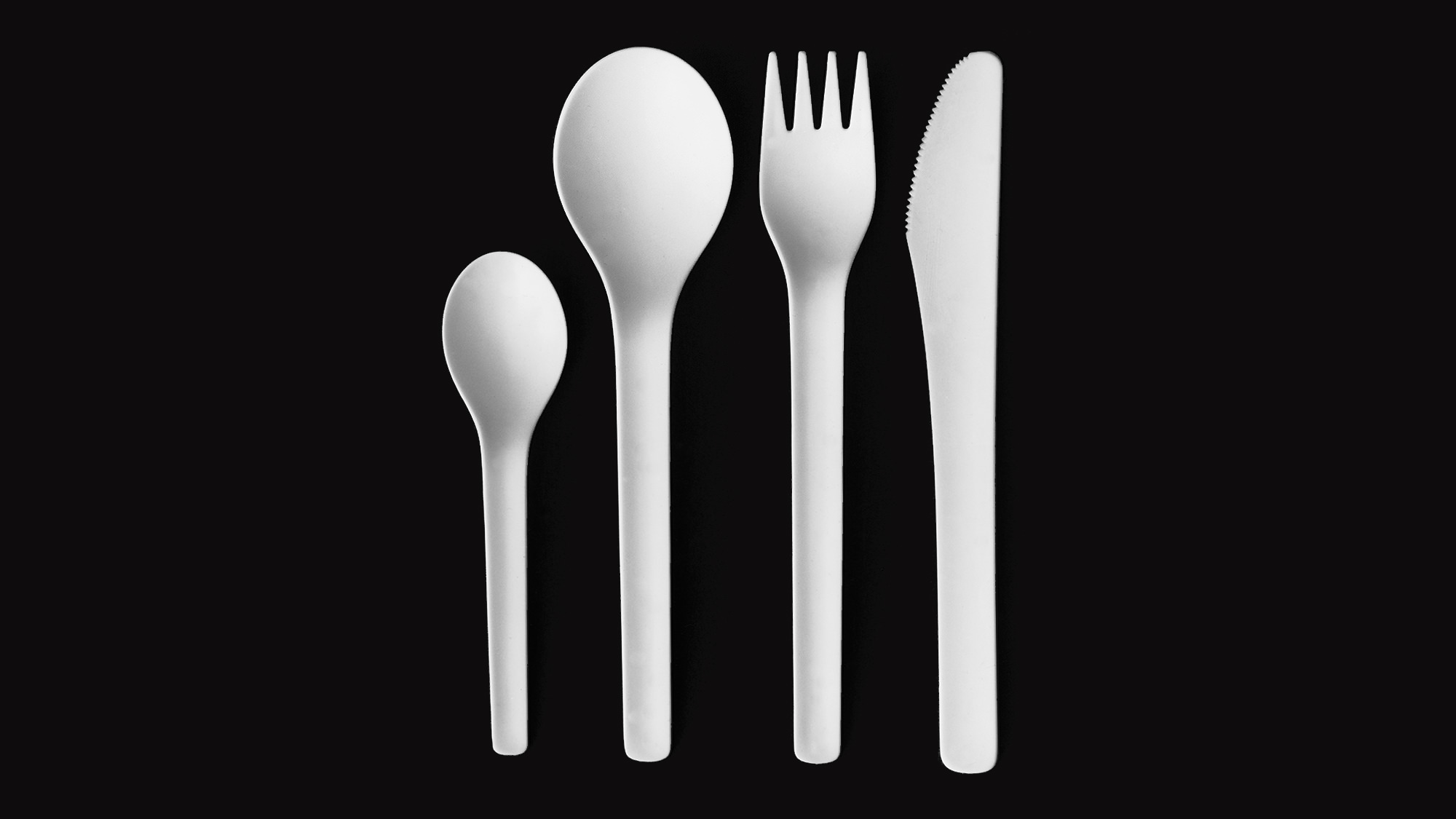 White plastic disposable cutlery on a black background.