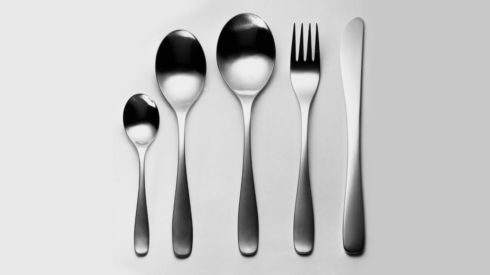 Thrift stainless steel cutlery items displayed in a line on a grey background.